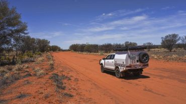 Outback vehicle on red dirt road with clear blue sky, perfect for Australian road trips and adventur.
