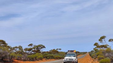 Australian outback road trip with campervan under blue sky.