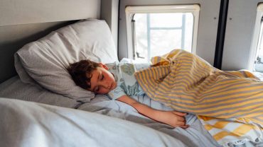 Child sleeping peacefully in a camper van bed with sunlight through the window.