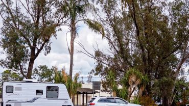 Caravan and vehicle parked in a natural outdoor environment with trees and cloudy sky.
