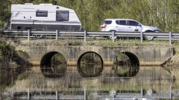 Scenic view of a bridge with three arches over a waterway, with a car and caravan traveling on the r.