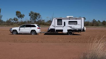 Caravan and car parked on a dirt road in the Australian outback under a clear blue sky.