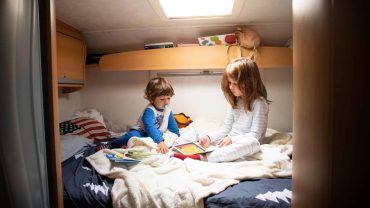 Two children reading books together on a camper bed in a cozy RV interior.