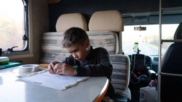 Child doing homework at a table inside a campervan during travel.