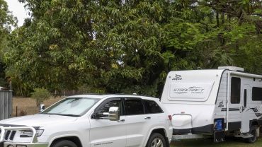 White SUV towing a caravan in a lush green outdoor setting.