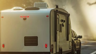 Travel trailer hitched to a car on scenic road.
