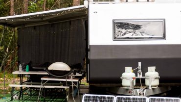 RV with solar panels and outdoor cooking area in a natural environment.