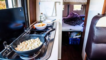 RV kitchen with stove and sleeping bunks in the background.