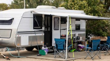 Caravan with outdoor camping gear and chairs at a campsite.