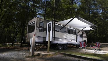 Modern caravan with awning set up in a wooded camping area.