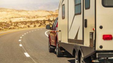 RV towing a caravan on an open road in the desert.
