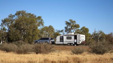 Car and caravan parked in a rural landscape with trees and dry grass.