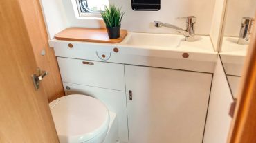 Toilet and sink in a compact bathroom with a small window and potted plant.