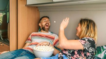 Happy couple enjoying popcorn inside a camper van during a road trip.