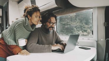 Travelers using a laptop inside a campervan or RV.