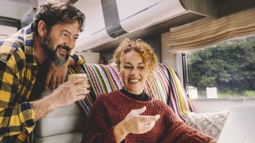 RV travel couple using laptop and phone.