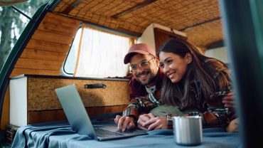 Camping couple using a laptop inside a camper van, enjoying outdoor adventure.