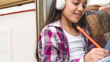 Young girl with headphones reading a Bible at home.