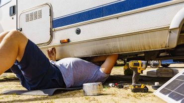 Person repairing or inspecting a caravan with tools and equipment nearby.