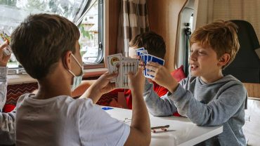 Kids playing cards inside a campervan, enjoying family camping and outdoor adventure.