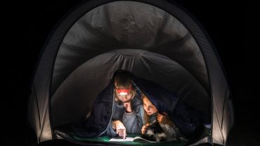 Camping with kids and a dog inside a tent at night, enjoying reading and exploring outdoors.