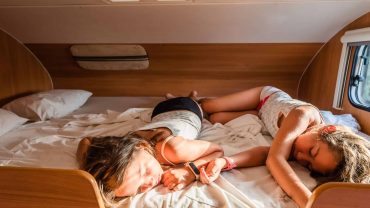 Kids sleeping on a bed inside a campervan or RV during camping.
