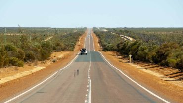 Long straight road through Australian outback with vehicle in distance.