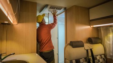 Travel van interior with a person reaching for the air conditioning unit, showcasing compact living.