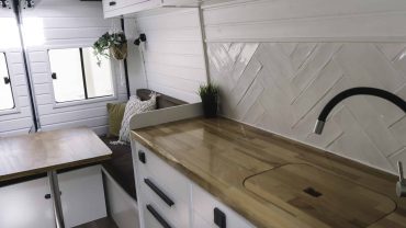 Modern tiny home kitchen with wooden countertop and white cabinetry.