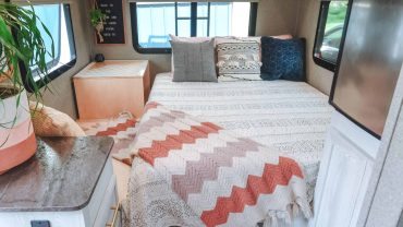 Cozy RV bedroom with a neatly made bed, decorative pillows, and ample storage in a compact space.