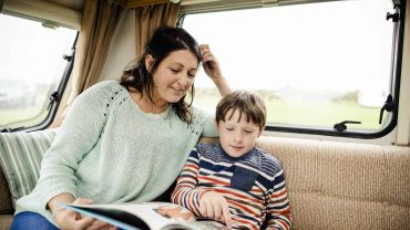Family reading a book together inside a campervan during travel.