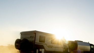 Sunset scene with a camper van driving across a dusty landscape at dusk. Perfect for outdoor travel.