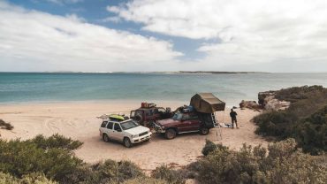 Beach camping with four-wheel drive vehicles and tents on the coast.