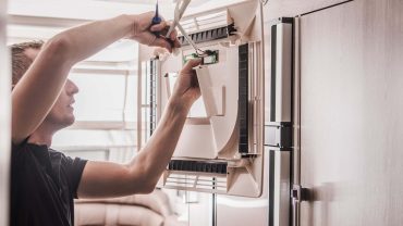 Refrigerator repair technician working on the fridge in a modern kitchen.
