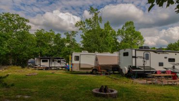 RVs parked at Big Lap Bible camping site with lush green trees and a partly cloudy sky.