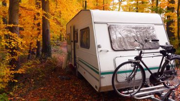 Caravan in autumn forest with bike, perfect for outdoor camping and adventure.