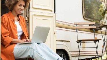 Camping van with woman working on a laptop outside in nature.
